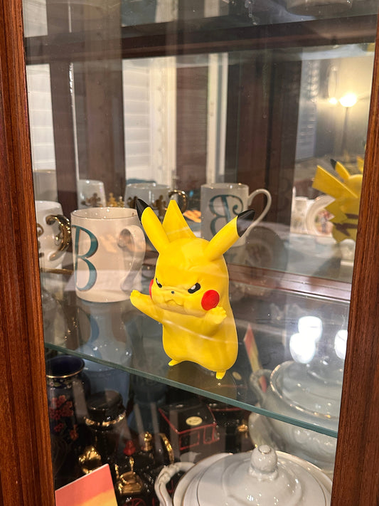 Yellow Pikachu figurine on a glass display case with reflections.